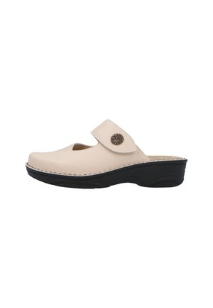Beige slip-on sko med sort sål, justerbar rem med en dekorativ rund metal knap på siden.
