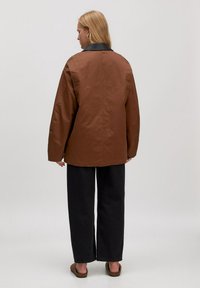 Bruine buitenjas met een zwarte leren kraag, met een losse pasvorm en lange mouwen, gecombineerd met zwarte wijde broek.