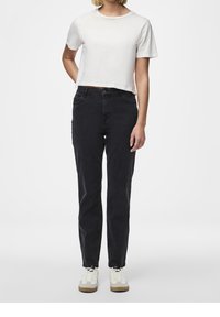 Svarta rakbenade byxor parades med en kort vit t-shirt. Outfiten kompletteras av vita sneakers med bruna detaljer.