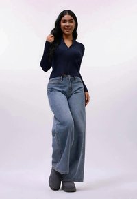 Top de manga longa em azul-marinho canelado, combinado com jeans claros de perna larga e cintura alta, e calçado cinza. Design simples com um corte descontraído.