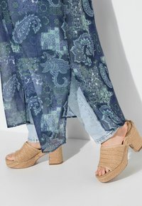 Průhledný, vzorovaný kimono v odstínech modré a zelené, vrstvené přes světle modré džíny; spárované s hnědými tkanými platformovými podpatky.