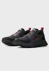 Un par de zapatillas deportivas negras y gris oscuro con acentos en rosa, suelas texturizadas y cordones reflectantes, posicionadas una al lado de la otra sobre un fondo blanco.