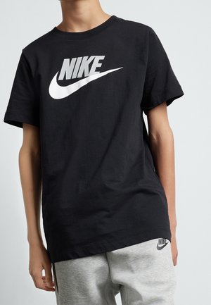 Person iført en sort Nike t-shirt med stort hvidt logo og lysegrå joggingbukser med lille Nike-logo på venstre lår.