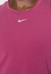 Fioletowy sportowy tank top wykonany z gładkiego materiału, z klasycznym okrągłym dekoltem i małym białym logo Nike w kształcie łyżwy na piersi.