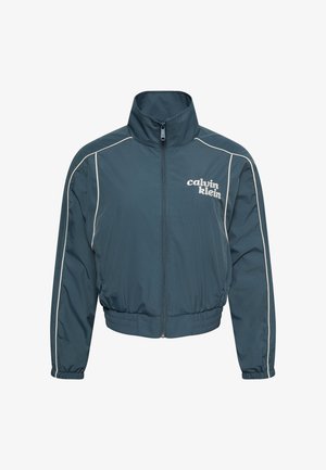 Chaqueta verde azulado oscuro con cremallera y cuello alto, ribetes blancos a lo largo de las mangas, cintura y puños elásticos, y logo "calvin klein" en el pecho izquierdo.
