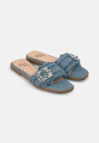 Sandali in denim con cinturini di tessuto sfrangiati, dettagli in fibbia argentata, suole piatte e suola marrone chiaro. Design con punta aperta.