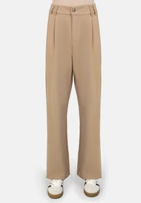 Beige wijde broek met hoge taille, voorzien van voorplooien en een enkele knoopsluiting. In combinatie met witte sneakers.