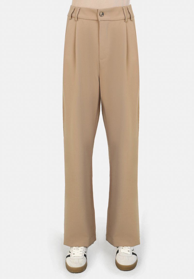 Beige wijde broek met hoge taille, voorzien van voorplooien en een enkele knoopsluiting. In combinatie met witte sneakers.