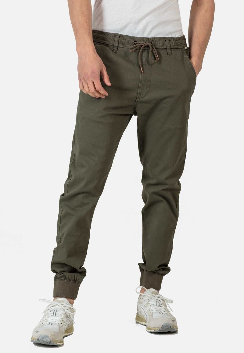 Olijfgroene joggerbroek met elastische tailleband en boorden, voorzien van een trekkoordsluiting en zijzakken. G gedragen met witte sneakers.