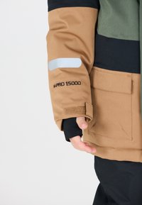Brun og grøn vejrbestandig jakke med reflekterende detaljer, justerbare manchetter og sort inderside. Har "W-PRO 15000" label.