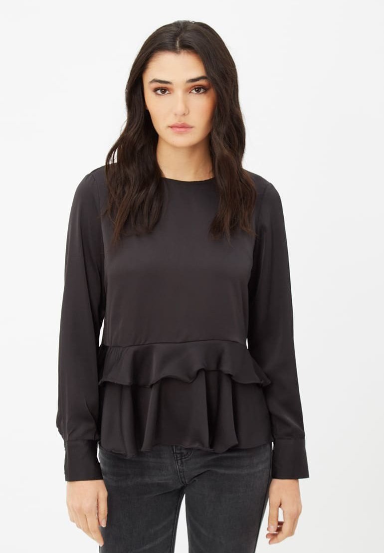 Blusa negra de manga larga hecha de tela suave, con un dobladillo en capas y con volantes. Cuello simple y puños abotonados. Llevada con jeans oscuros.