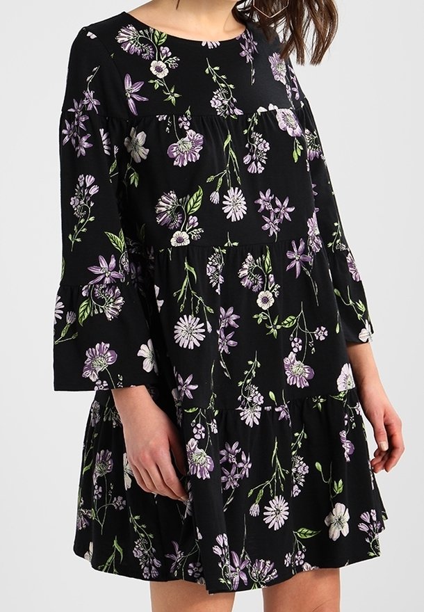 Czarna sukienka w kwiaty z rękawami o długości trzy czwarte w kształcie dzwonka, zdobiona purpurowymi i białymi wzorami kwiatowymi, z falbaniastym dołem i luźnym krojem.