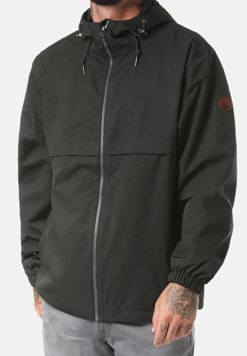 Mörkgrön jacka med dragkedja och huva, elastiska muddar och en bröstficka. Har en logotypmärke på vänster ärm och en slät yta.