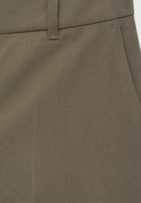 Close-up van kaki stof met tailleband, riemlus en naaddetails op een paar broeken.