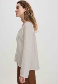 Top a maniche lunghe in lino beige chiaro con scollatura rotonda e dettaglio con cordoncino davanti. Vestibilità leggermente morbida e tessuto testurizzato.
