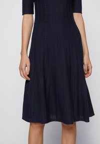 Mörkblå stickad klänning med korta ärmar, med vertikal ribbning och texturerade paneler. Utloppskjol med ett subtilt, elegant mönster.