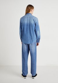 Camicia in denim azzurro chiaro con yoke sul retro, polsini con bottoni e orlo curvo. Abbinata a jeans azzurri chiari a vestibilità ampia e sneakers nere.