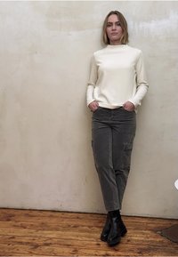 Kermainen neulepaita korkealla kaula-aukolla, yhdistetty harmaisiin cargo-housuihin. Mustat nilkkurit viimeistelevät asun. Yksinkertainen, rento muotoilu.