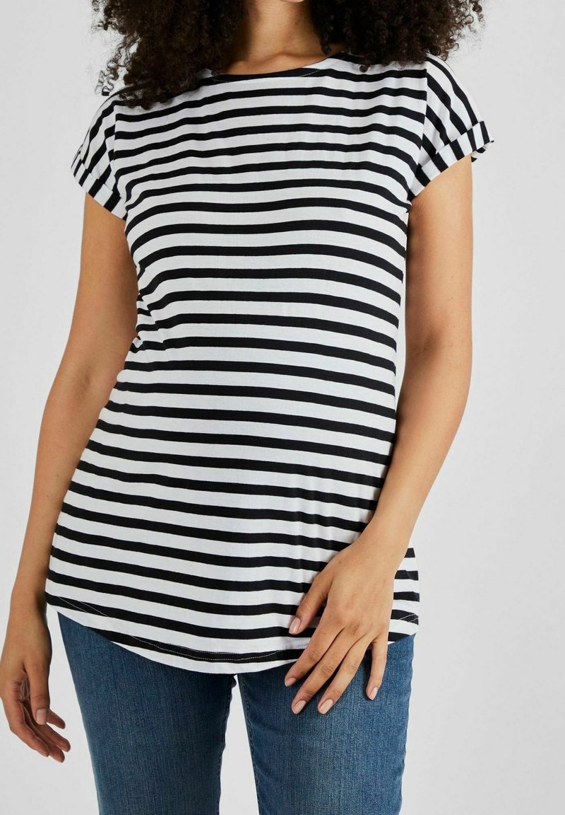 Femme portant un t-shirt rayé noir et blanc à manches courtes et un jean bleu, main posée sur la hanche, torse visible.