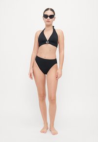 Zwart bikiniset met een halternekdesign, zilveren hardware-details in het midden en een hoogbuis onderstuk, tegen een neutrale achtergrond.