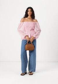 Rosa schulterfreie Bluse mit Blumendruck, elastischem Oberteil und puffärmel, kombiniert mit weiten Jeans und einer kleinen braunen Handtasche.