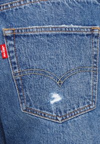 Levi's denimjeans bakficka, blått tyg med en slitna design, med orange sömmar och en röd Levi's logotags.