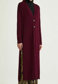 Cardigan long bordeaux en tissu doux, avec un col en V, des manches longues et deux boutons argentés sur le devant.