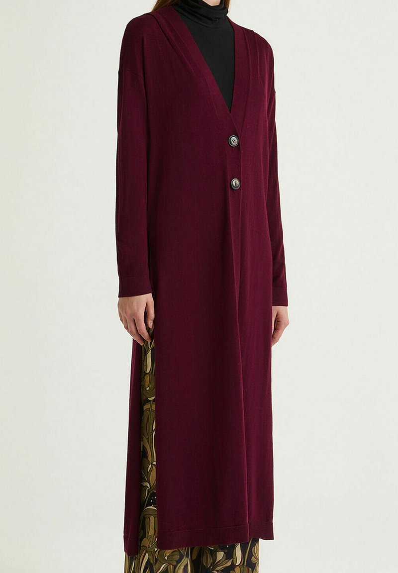 Cardigan long bordeaux en tissu doux, avec un col en V, des manches longues et deux boutons argentés sur le devant.