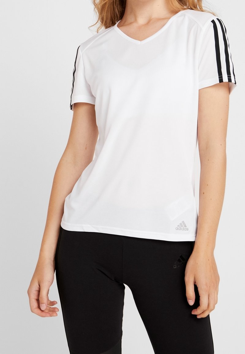 Camiseta deportiva blanca con escote en V, mangas cortas a rayas negras y un pequeño logo gris en el dobladillo. Tejido suave y ligero.