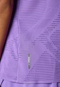 Camiseta deportiva morada con un tejido texturizado y transpirable, que presenta perforaciones y una etiqueta lateral que dice "ACTIBREEZE."