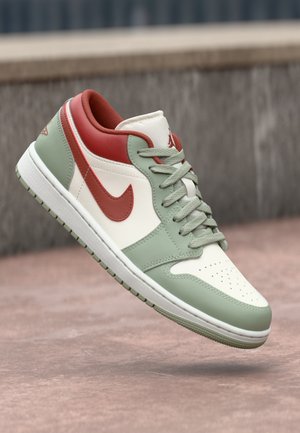 Low-top sneaker with white, green, and red panels, green laces, and a red Nike swoosh, floating above a pinkish textured surface.