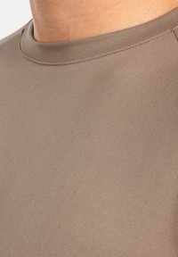 Camisa de manga corta en un color topo claro con una textura suave y lisa, y un diseño clásico de cuello redondo. Detalle de costura visible en los hombros.