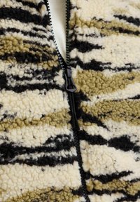 Tejido de forro polar texturizado en rayas crema, oliva y negro, que cuenta con un cierre de cremallera en la parte frontal, con una apariencia suave y mullida.