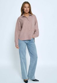 Light pink, textured, button-up shirt with a collar, paired with light blue wide-leg jeans and black pointed-toe shoes.