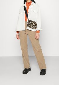 Korsryggväska i leopardmönster med en guldfärgad dragkedja, bärs med en vit texturerad jacka, en orange polotröja och beige kordbyxor. Svarta platåskor.