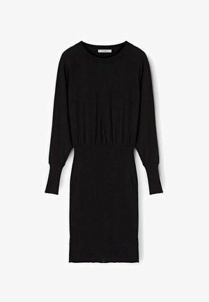 Czarna dzianinowa sukienka z długimi rękawami, okrągłym dekoltem i zbieranym w pasie, co podkreśla sylwetkę. Posiada prążkowane mankiety i akcenty u dołu.