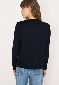 Navyblaues Langarmoberteil aus einem weichen Stoff mit lockerem Sitz, ausgestattet mit einem schlichten Rundhalsausschnitt und leicht heruntergesetzten Schultern. Kombiniert mit Jeans.