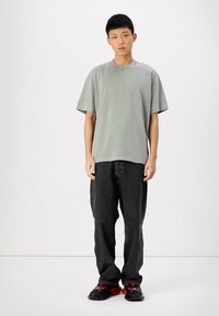 T-shirt oversized verde claro de algodão com mangas curtas, combinado com jeans de ganga pretos largos e sapatilhas pretas com detalhes vermelhos.