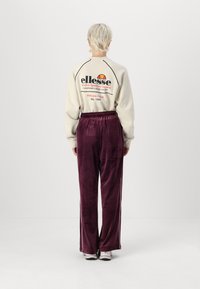 Creme sweatshirt med sort og rød logo tekst på ryggen; parret med bordeaux velourbukser med sidelister. Tekstureret stof, løst fit.