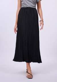 Black pleated maxi skirt with a lightweight texture and an elastic waistband, complemented by strappy black sandals.