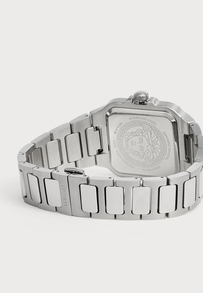 Montre-bracelet en acier inoxydable avec un boîtier rectangulaire, une tête de Méduse gravée au dos et un bracelet métallique relié fermé par une boucle.
