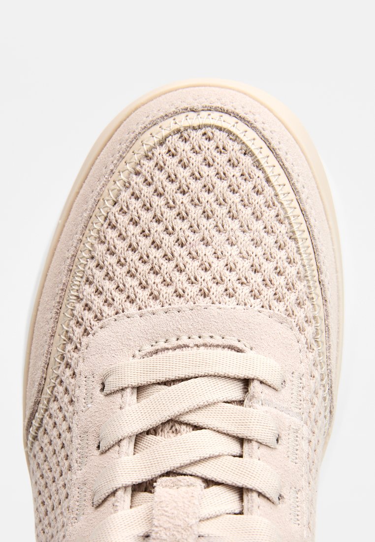 Helle beige Sneaker mit einem atmungsaktiven Mesh-Obermaterial, strukturierten Wildleder-Akzenten, flachen Schnürsenkeln und einer gepolsterten Sohle. Detaillierte Nähte entlang der Kante.