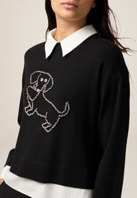 Czarny, krótki sweter z designem psa w rhinestonach, uzupełniony białą koszulą z kołnierzykiem pod spodem. Gładka tekstura i luźny krój.