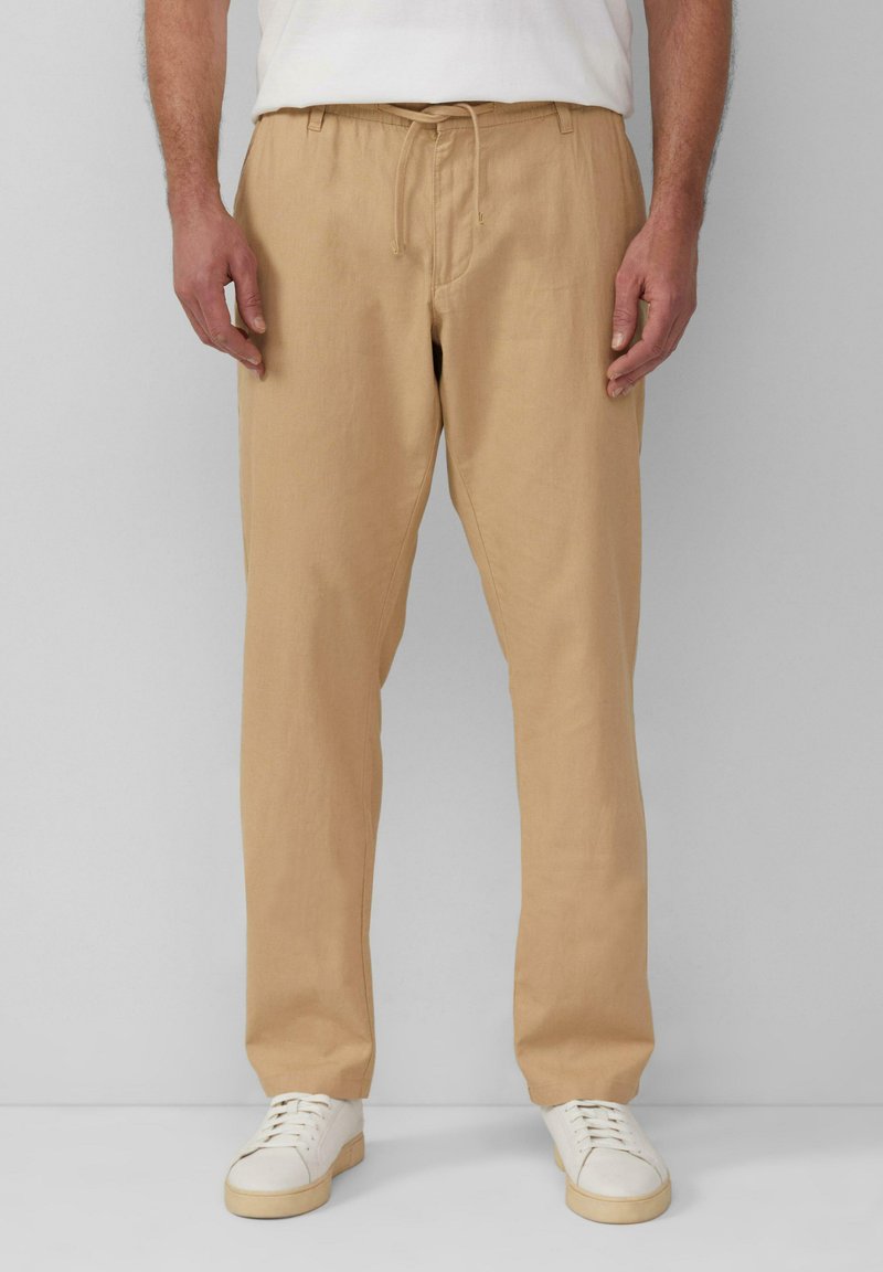 Beige linnen broek met een elastische tailleband en trekkoord. Recht voorgevormd ontwerp, gedragen met witte sneakers. De textuur lijkt glad en lichtgewicht.