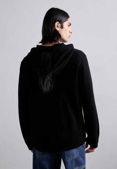 Schwarzer Kapuzenpullover mit einem strukturierten, faux-Fell-Schwanzdetail auf der Rückseite. Hergestellt aus einem weichen Material, mit einer lockeren Passform und langen Ärmeln.