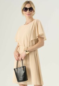 Abito midi color pesco con maniche a volants e vita regolabile con cordoncino. Indossato con una borsa nera texturizzata e occhiali da sole neri oversize.