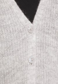 Lichtgrijze cardigan met een V-hals, gestructureerd breipatroon en twee ronde, grijze knopen aan de voorkant. Zacht, fluffy uiterlijk.