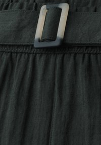 Zwarte stoffen rok met een geplooide taille en een rechthoekige doorschijnende zwarte riemgesp waar een bijpassende stoffen riem doorheen is gestrikt.