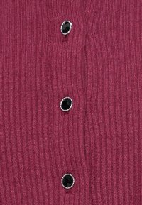 Tissu côtelé rose foncé avec trois boutons décoratifs noirs aux bords argentés disposés verticalement.