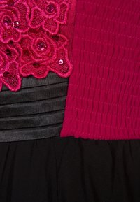 Fuchsia ovanliv med blommig spets och paljetter över en svart plisserad kjol, med en texturerad, rynkad design.